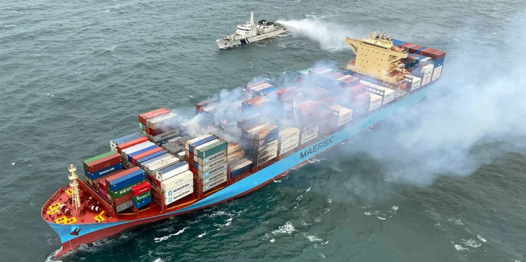Marie Maersk container ship on fire off the coast of Liberia, with firefighting tugs approaching.